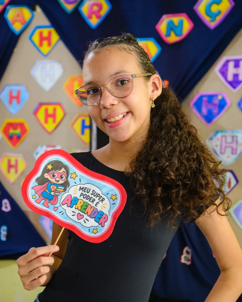 Estudante da CaHsi sorrindo e segurando a plaquinha "Meu super poder é aprender"