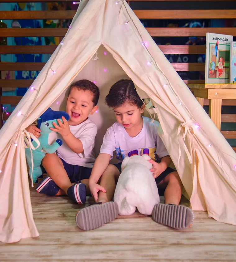 Duas crianças da Educação Infantil brincando dentro de uma cabana de tecido